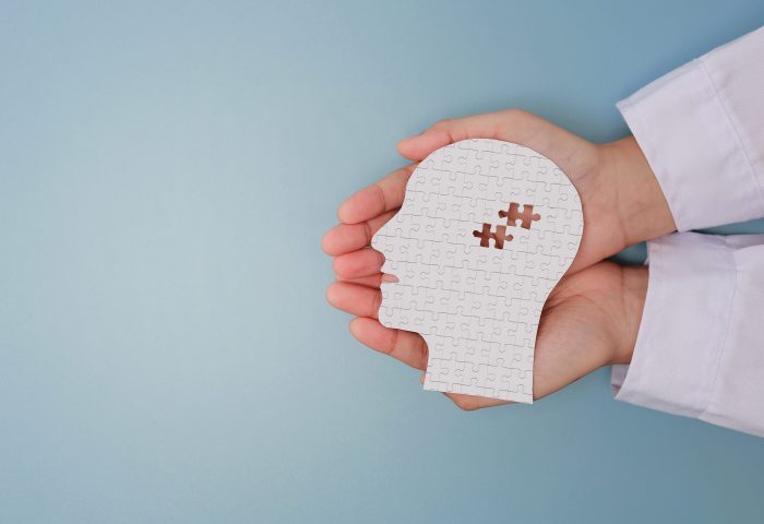 Caring doctor hand holding white paper head with puzzle piece showing visual mental health recovery concept offering gentle support Caring doctor hand holding white paper head with puzzle piece showing visual mental health recovery concept offering gentle support